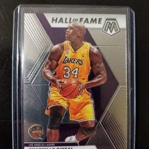 May include: A silver and purple basketball trading card featuring Shaquille O'Neal in a Los Angeles Lakers uniform. The card has a silver "Hall of Fame" inscription and a silver "M" logo.