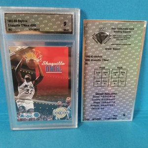 May include: A graded trading card of Shaquille O'Neal from the 1992-93 Skybox series. The card is in mint condition and has a grade of 9. The front of the card features a photo of O'Neal in his Orlando Magic uniform, while the back of the card includes information about his career and statistics.
