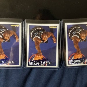 May include: Three trading cards featuring a basketball player in a blue and white uniform, with the text "SHAQUILLE O'NEAL ORLANDO MAGIC C" on each card.