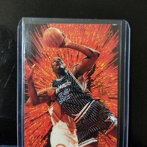 May include: A basketball trading card featuring Shaquille O'Neal in an Orlando Magic uniform, number 32. The card has a red and orange background with a burst design. The player is holding a Spalding basketball.