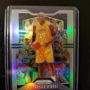 May include: A silver and purple basketball trading card featuring a photo of Shaquille O'Neal in a Los Angeles Lakers uniform. The card is from the Panini Prizm collection.