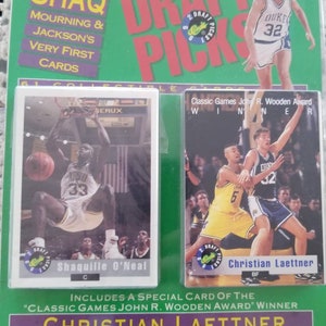 Könnte beinhalten: Versiegeltes Basketball-Kartenset mit Shaquille O'Neal und Christian Laettner. Die Verpackung ist grün mit rotem und weißem Text, einschließlich "Shaq" und "Draft Picks". Die Karten zeigen Actionaufnahmen der Spieler.