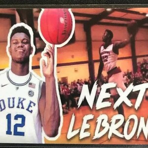 Pu&ograve; includere: Un giocatore di basket che indossa una maglia bianca Duke con il numero 12, tiene una palla da basket nella mano destra. Il testo "NEXT LEBRON?" &egrave; scritto in bianco su uno sfondo rosso e arancione.