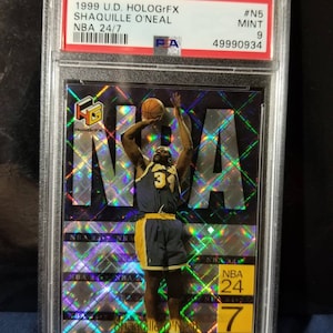 May include: A 1999 U.D. HoloGrFX Shaqille O'Neal NBA trading card, graded a 9, with a holographic background and a picture of Shaq in a basketball uniform.