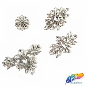 May include: Four crystal rhinestone embellishments in different shapes and sizes. The embellishments are on a white background.