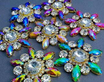 May include: Assortment of iridescent rainbow colored rhinestones with gold settings. The rhinestones are in various shapes and sizes, including round, oval, and teardrop.