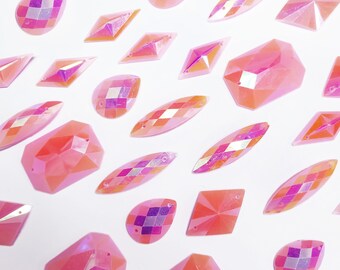 May include: Assortment of pink iridescent plastic gem shapes. The gems are in various sizes and shapes, including ovals, diamonds, and rectangles.