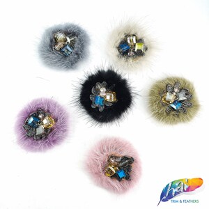 May include: Six faux fur pom poms with jeweled embellishments. The pom poms are in various colors including black, gray, pink, purple, and green.