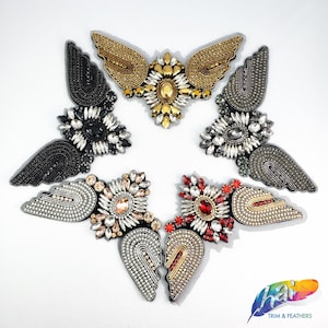 May include: Six different embroidered patches in the shape of wings with various colored rhinestones and beads. The patches are arranged in a star shape on a white background.