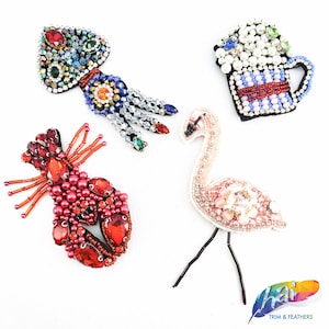 Può includere: Quattro toppe ricamate colorate che rappresentano un'aragosta rossa, un fenicottero rosa, una boccale di birra blu e bianca e una medusa multicolore.