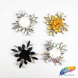 May include: Four different flower embellishments with rhinestones. The flowers are white, black, yellow, and iridescent. The embellishments are perfect for adding a touch of sparkle to any project.