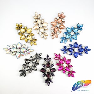 May include: Assortment of rhinestone embellishments in various colors, including gold, silver, pink, blue, purple, and black. Each embellishment features a cluster of rhinestones in a leaf-like design.