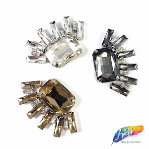 May include: Three sets of rhinestone embellishments with a rectangular shaped stone in the center and smaller rhinestones surrounding it. The stones are clear, gold, and black.