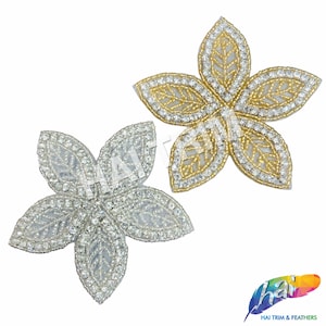 May include: Two silver and gold flower-shaped embellishments with rhinestone accents. Each flower has five petals with a leaf design.