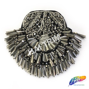 Puede incluir: Aplique bordado negro y plateado con un diseño en forma de abanico. La parte superior está densamente cubierta de pequeñas cuentas redondas, mientras que la parte inferior presenta cuentas más grandes en forma de cono. El aplique es probablemente para embellecer ropa o accesorios.