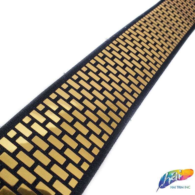 May include: Black elastic trim with a gold geometric pattern. The pattern is made up of small, rectangular shapes.