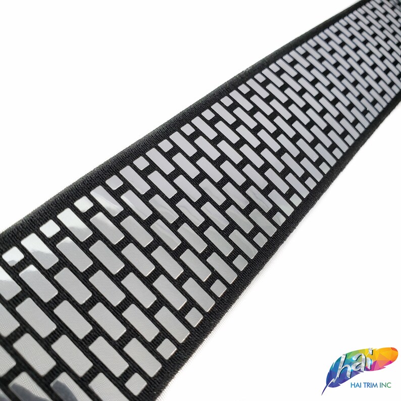 May include: Black elastic trim with a silver reflective pattern of small rectangles. The trim is approximately 1 inch wide.