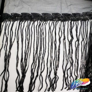 May include: Black fringe trim with sequins. The fringe is made of small black beads and the sequins are scattered throughout the fringe.