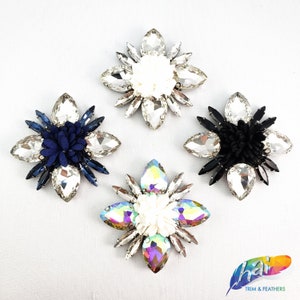 May include: Four decorative crystal flower embellishments with different colored centers. The centers are white, blue, black, and iridescent.
