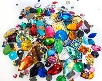Puede incluir: Un gran surtido de piedras de imitación y gemas de vidrio de colores en varias formas y tamaños. Las gemas están esparcidas sobre un fondo blanco.