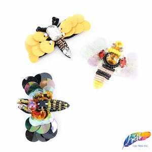 Puede incluir: Tres parches de hierro bordados con una abeja, una mariposa y una libélula. La abeja es amarilla y negra con diamantes de imitación rojos y transparentes. La mariposa es amarilla con diamantes de imitación transparentes. La libélula es iridiscente con lentejuelas negras y doradas.