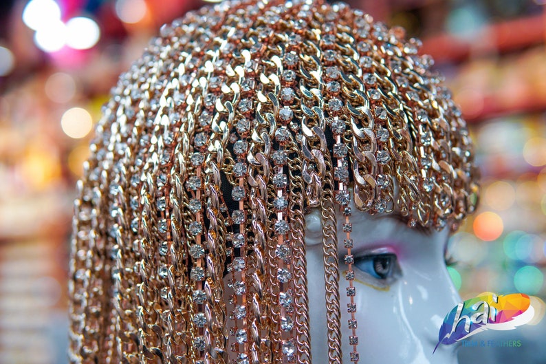 Op de afbeelding: Een gouden kettinghoofdtooi met strass. De hoofdtooi is gemaakt van meerdere kettingen die aan elkaar zijn verbonden. De kettingen zijn versierd met kleine, heldere strasssteentjes.