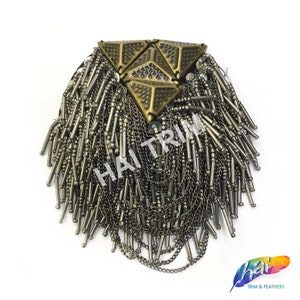 May include: A gold-toned metal embellishment with a geometric design and a fringe of metal chains and beads.