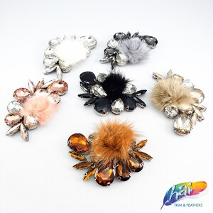 May include: Assortment of six rhinestone and faux fur embellishments. Each embellishment features a cluster of rhinestones with a small faux fur pom-pom in the center. The embellishments are in various colors, including black, brown, white, and clear.