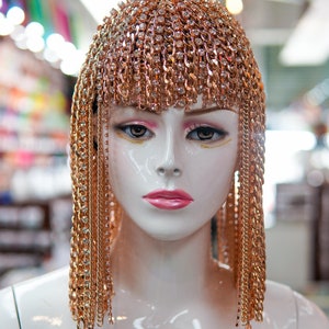 Op de afbeelding: Een mannequinhoofd met een gouden kettinghoofdtooi met strass. De hoofdtooi is gemaakt van veel kleine kettingen die tot aan de schouders hangen. De hoofdtooi is een haaraccessoire.