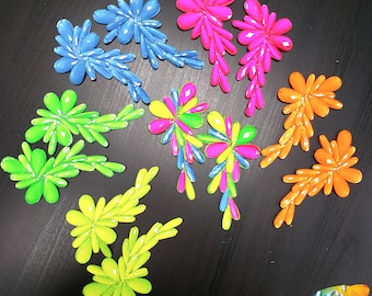 May include: Assortment of colorful, flower-shaped embellishments. The embellishments are made of plastic and have a glossy finish. They are available in a variety of colors, including pink, blue, green, and yellow.