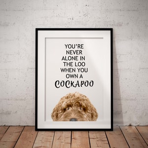 May include: A white framed print with the text "You're never alone in the loo when you own a Cockapoo" and a brown Cockapoo dog peeking over the top of the frame.