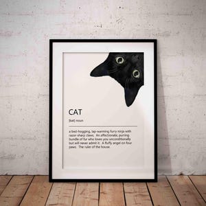 Peut inclure: Une affiche encadrée avec un chat noir regardant par le haut. Le mot "CAT" et une définition du chat sont affichés. L'affiche est dans un cadre noir, sur fond blanc, posée sur un sol en bois.