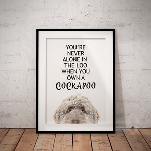 May include: A white framed print with a black and white illustration of a Cockapoo dog. The text on the print reads "You're never alone in the loo when you own a Cockapoo."