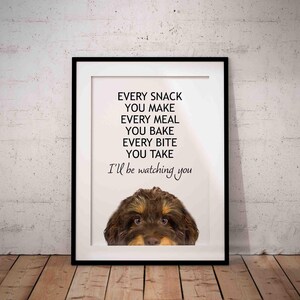 May include: A framed print featuring a brown and white dog peeking out from the bottom. The text on the print reads "Every snack you make, every meal you bake, every bite you take, I'll be watching you."