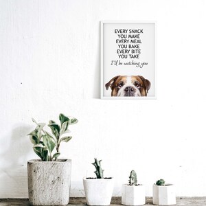 May include: A white framed print with a bulldog's head peeking out from the bottom. The text reads "Every snack you make, every meal you bake, every bite you take, I'll be watching you."