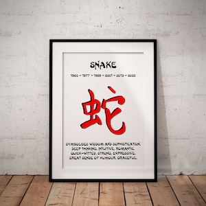 May include: A white framed print with black text that reads "SNAKE" and "1965-1977-1989-2001-2013-2025". The Chinese character for snake is in red and the text below reads "SYMBOLISES WISDOM AND SOPHISTICATION. DEEP THINKING, INTUITIVE, ROMANTIC, QUICK-WITTED, STRONG, EXPRESSIVE, GREAT SENSE OF HUMOUR, GRACEFUL."