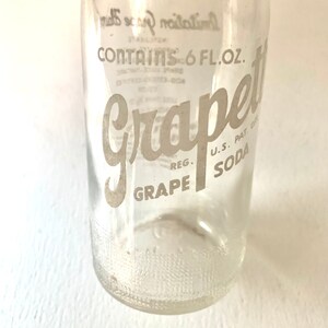 Puede incluir: Una botella de vidrio transparente con una etiqueta blanca que dice "Grape Soda" y "Contains 6 FL. OZ."