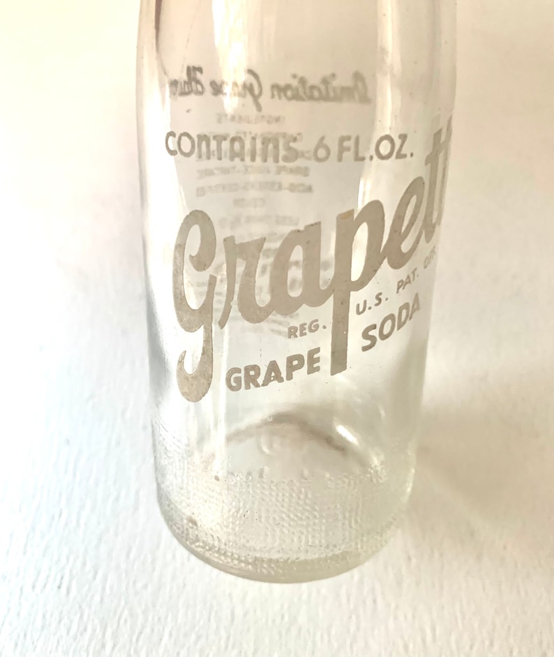Puede incluir: Una botella de vidrio transparente con una etiqueta blanca que dice "Grape Soda" y "Contains 6 FL. OZ."