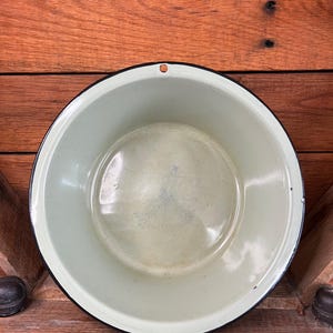 May include: A vintage green enamelware bowl with a black rim. The bowl is empty and has a smooth, shiny surface.