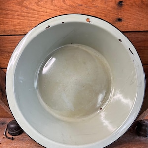 May include: A vintage green enamelware bowl with a black rim. The bowl has some minor chips and scratches on the surface.