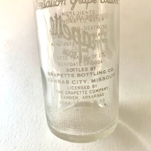 Puede incluir: Una botella de vidrio transparente con una etiqueta blanca que dice "Citation Grape Flavor". La etiqueta enumera los ingredientes, que incluyen agua carbonatada, az&uacute;car, dextrosa, jugo de uva, &aacute;cido tart&aacute;rico y color certificado. La botella est&aacute; embotellada por Grapette Bottling Co. en Kansas City, Missouri.