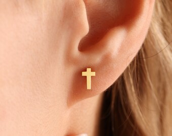 May include: A gold cross stud earring worn in a person's earlobe.