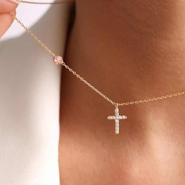 May include: A gold chain necklace featuring a small cross pendant encrusted with clear stones and a single round pink stone set along the chain. The delicate metal links connect the cross and the pink stone, creating a refined and simple jewellery piece.