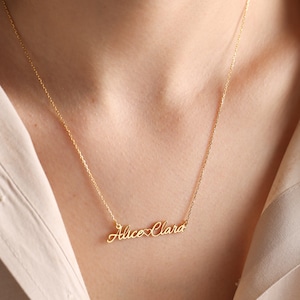 May include: Gold necklace with a delicate chain and a personalized nameplate pendant that reads "Alice Clara" with a heart symbol between the names.