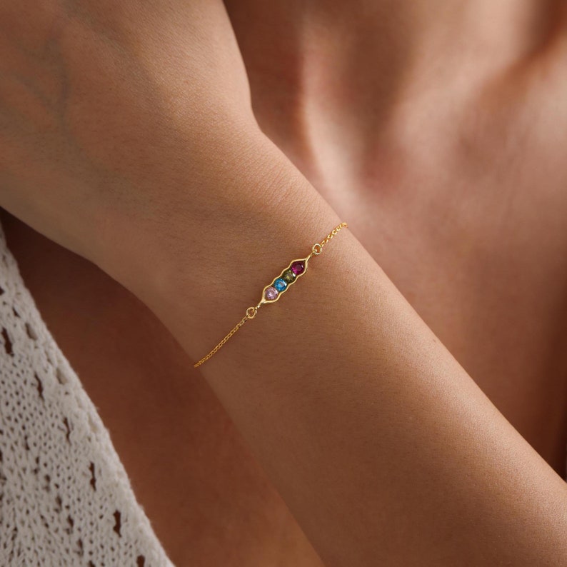 May include: A gold chain bracelet with a pea pod charm featuring five colorful gemstones.
