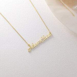 May include: A gold necklace with the names "Alice" and "Clara" connected by a heart symbol.