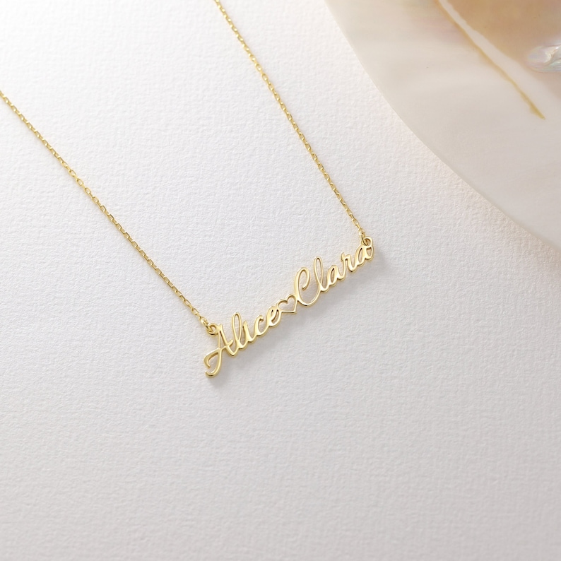 May include: A gold necklace with the names "Alice" and "Clara" connected by a heart symbol.