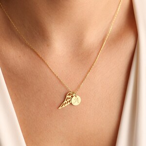 Puede incluir: Un collar de oro con una cadena delicada y un colgante que presenta un ala de &aacute;ngel individual y un peque&ntilde;o disco redondo con la letra 'A' grabada.