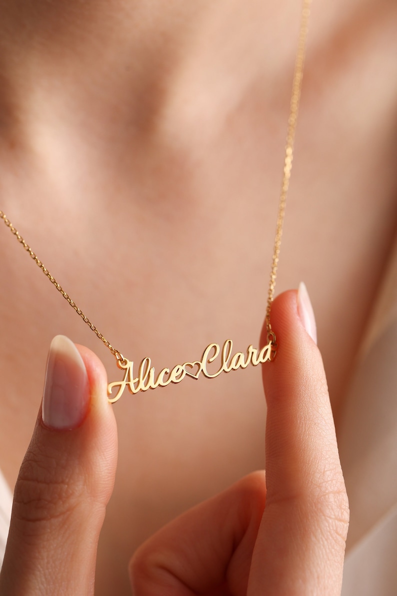 May include: Gold necklace with the names "Alice" and "Clara" separated by a heart symbol.