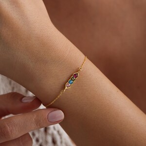May include: A gold chain bracelet with a pea pod charm featuring five colorful gemstones.